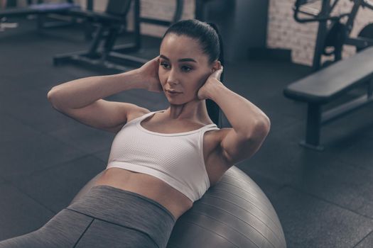 Beautiful fit woman doing abs crunches on fitness ball, working out at the gym. Attractive fitness female exercising, doing abdominal crunches. Sportswoman training at gym studio. Sports, body care concept