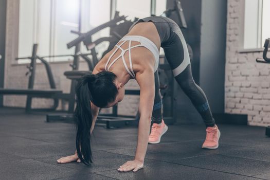 Dark haired fit sportswoman stretching her body before workout at the gym, copy space. Fitness female exercising at sports studio, doing yoga. Flexible female stretching her back, copy space