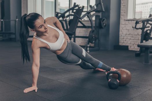 Full length shot of a beautiful dark haired athletic woman exercising at the gym, doing side plank, copy space. Young sportswoman with fit and toned body working out. Health, sports motivation concept