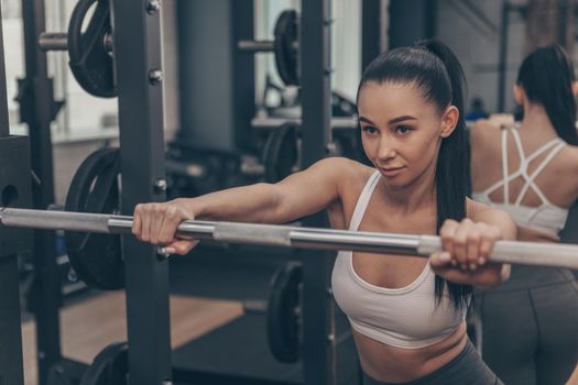 Confident young fitness woman looking concentrated, preparing for her barbell workout. Beautiful healthy female athlete focusing before lifting weights at gym sports studio, copy space