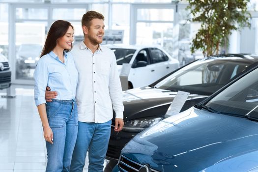 Making their choice. Beautiful young loving couple smiling happily as they are choosing a car at the local dealership