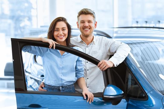 Perfect family car. Shot of a beautiful happy couple posing together behind an open door of a new car they just bought at the dealership smiling to the camera joyfully