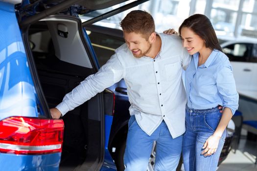 Tons of space here. Shot of a beautiful happy couple checking out the trunk of a new car at the dealership looking inside smiling joyfully