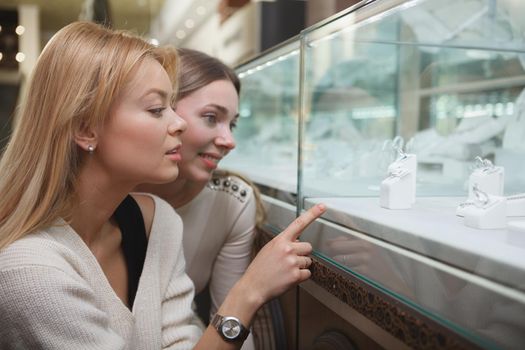 Close up of two beautiful women choosing jewelry to buy from retail display