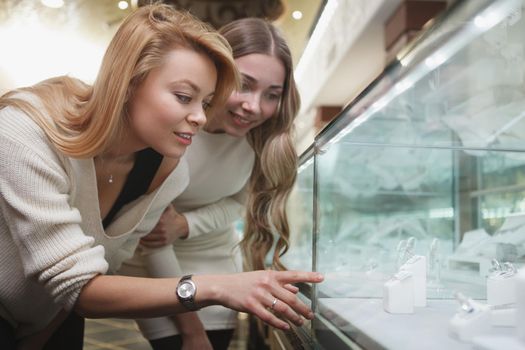 Two female customers looking at jewelry on sale on retail display at jewelry store