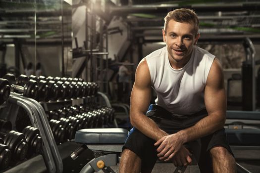 After gym session. Cheerful handsome young fitness man sitting relaxed at the gym after his workout smiling joyfully copyspace motivation confidence sports lifestyle happiness active people concept