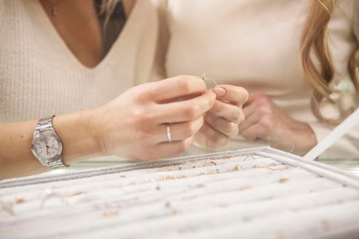 Unrecognizable female friends choosing rings to buy at jewelry store