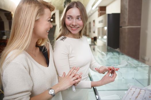 Cheerful woman talking to her friend while choosing jewelry to buy