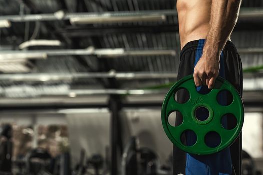 Sports challenge. Cropped shot of a shirtless athletic man with toned body and six-pack abs holding barbell weight plate standing in the gym studio copyspace fitness weightlifting workout exercising