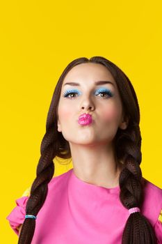 Beauty girl with funny make-up in doll costume on yellow background