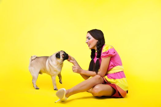 cute girl in doll dress feed a dog with cheese on yellow background