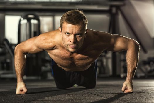 No way back. Handsome young serious motivated fitness man looking to the camera confidently doing pushups at the gym workout muscular power strength endurance energy sport health challenge concept