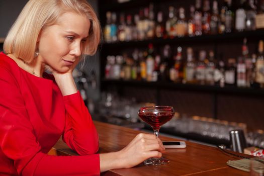 Cropped shot of a sad woman drinking at the bar. Depressed woman having a cocktail alone at the restaurant
