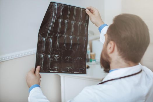 Rear view shot of unrecognizable male doctor lookign at mri scans of a patient, copy space. Male doctor working at the hospital, examining x-ray scans. Illness, disease, therapy concept