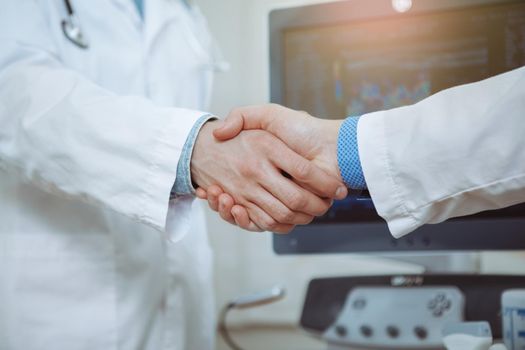 Cropped close up of two male doctors in labcoats shaking hands at the hospital, celebrating success. Male practitioner shaking hands with colleague at work. Medical team, achievement, science concept