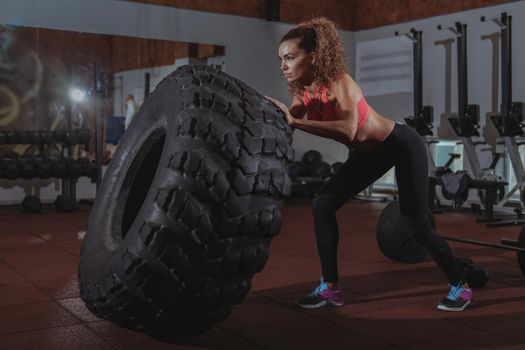 Stunning focused female crossfit athlete flipping huge heavy wheel, working out at crossfit box gym.Attractive sportswoman exercising at crossfit box gym