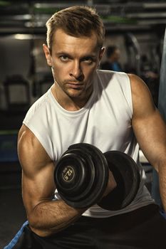 Strengthen your body. Vertical cropped shot of a young handsome athletic muscular man looking to the camera confidently working out with dumbbells at the gym biceps arms muscles toning shaping sports