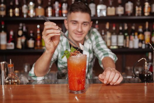 Close up of a delicious coktail with ice, professional bartender is decorating. Barman working at his restaurant, preparing a drink for customer