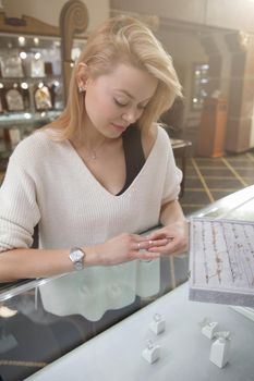 Vertical shot of a beautiful happy woman choosing ring to buy at jewelry store