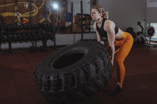 Young female crossfit athlete with strong toned body lifting heavy wheel, exercising at the gym. Attractive sportswoman working out at crossfit box gym, copy space