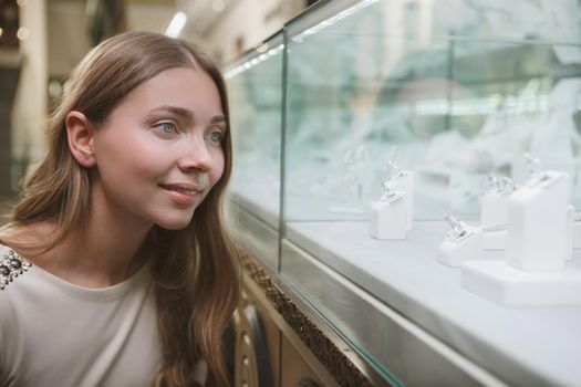 Charming woman smiling, looking at jewelry store retail display