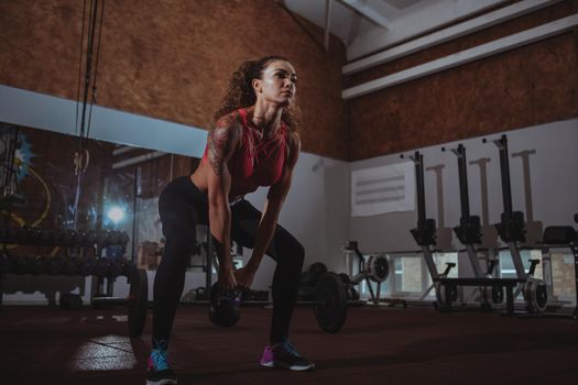 Full length shot of a beautiful muscular crossfit female athlete doing kettlebell swings, exercising at the gym. Low angle shot of a sportswoman working out with weights, copy space