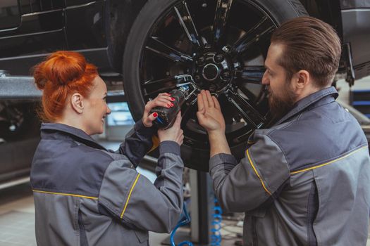 Bearded male mechanic helping his female colleague torquing the lug nuts of a car on a lift at the garage. Female professional car technician enjoying working at car service station