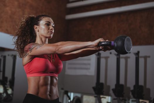 Attractive female crossfit athlete working out with kettlebell at the gym. Beautiful sportswoman with perfect fit body lifting kettlebell at crossfit box gym