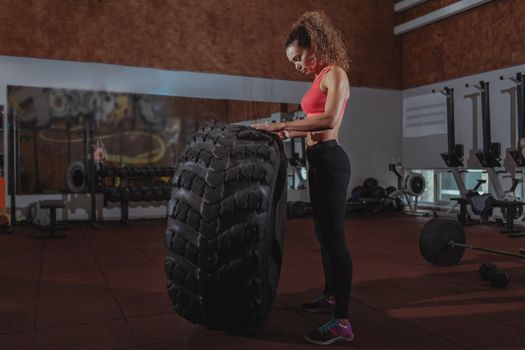 Full length of a beautiful athletic woman resting after flipping huge heavy tire, exercising at crossfit box gym. Attractive female crossfit athlete relaxing after training, copy space