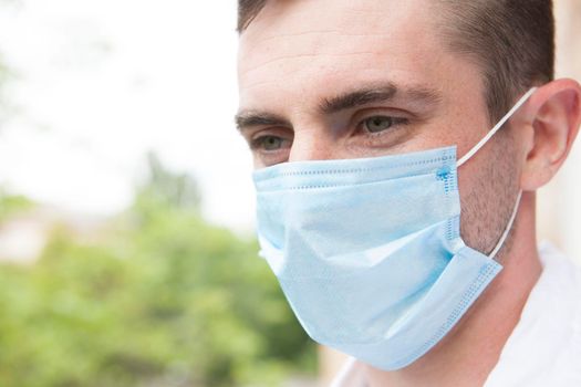 Close up of a man with beautiful eyes wearing medical protective mask, looking away outdoors