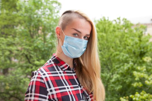 Stylish woman looking to the camera, wearing protective mask outdoors. Pollution, virus concept