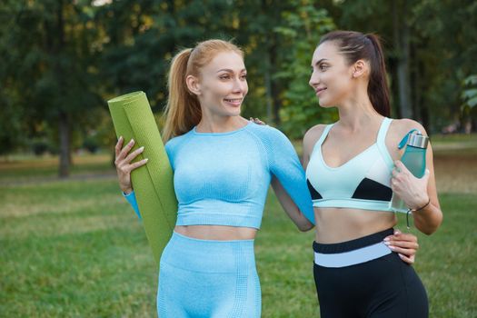 Happy healthy female friends walking in the park after outdoor workout, smiling and chatting joyfully