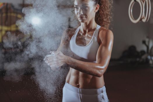 Cropped shot of a beautiful sportswoman with perfect abs and fit toned body clapping hands with magnesium. Female crossfit athlete chalking hands before weighlifting