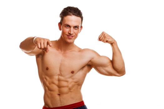 Handsome young ripped bodybuilder flexing his muscles smiling cheerfully pointing to the camera. Sexy athletic healthy man showing his biceps isolated, copy space. Gym, lifestyle, motivation concept