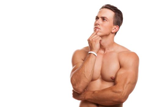 Young attractive bodybuilder posing shirtless isolated, copy space. Handsome athletic man looking away thoughtfully rubbing his chin. Sportsman thinking. Muscular man making decision. Health concept