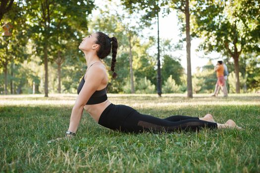 Athletic young woman exercising outdoors in the park, doing cobra asana