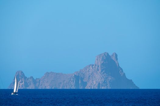 White sailboat sailing the sea with Es Vedra in the background