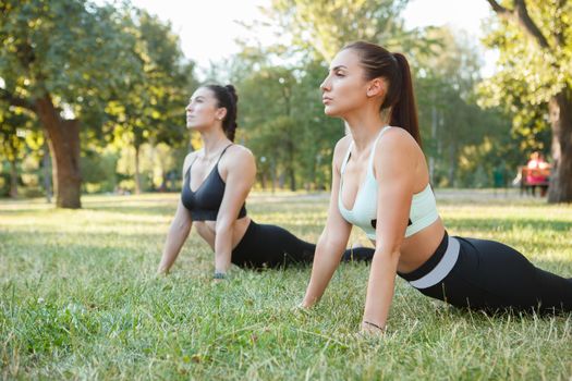 Two attractive young women enjoying practicing yoga outdoors on sunrise