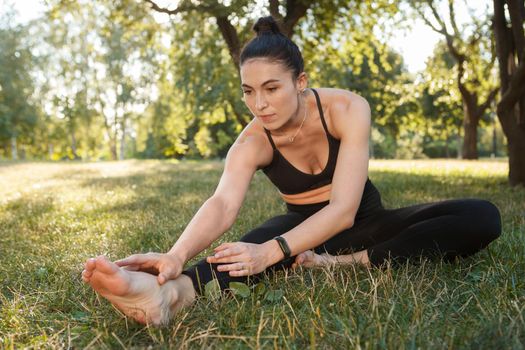 Young athletic woman working out at the park, stretching on the grass