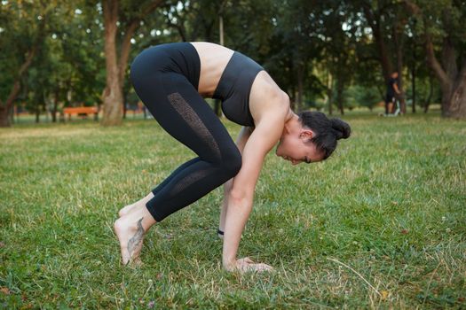 Fit young woman doing crow asana, practicing yoga outdoors at the park