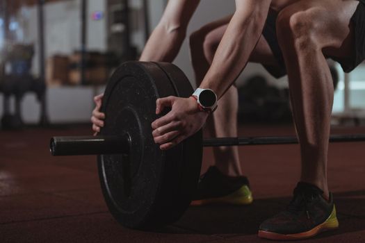 Cropped close up of unrecognizable male crossfit athlete adding weight plates on his barbell. Sportsman preparing for his weighlifting workout at crossfit box gym