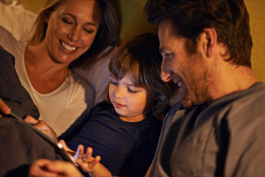 Family entertainment before bedtime. a young family lying in bed and looking at a digital tablet