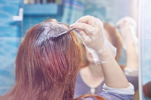 a woman dyes her hair red, coloring the hair roots with henna or dye.