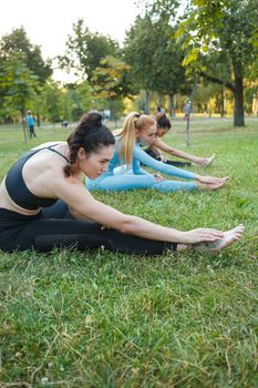 Vertical shot of three young women stretching outdoors, doing yoga together at the park