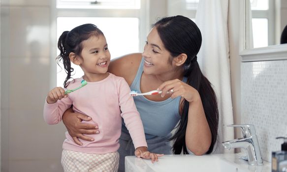 Mother with girl learning to brush teeth with toothbrush together in bathroom for oral or dental wellness. Happy, love and care mom teaching child or kid about dentistry and cleaning mouth in morning.