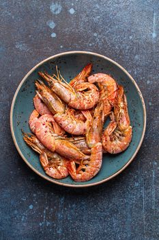 Whole fried big shrimps with seasonings in blue bowl on stone rustic background from above. Fresh cooked delicious grilled shrimps served on plate top view, healthy seafood meal