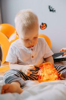 Children's Halloween - a boy in a carnival costume with orange and black balloons at home. Ready to celebrate Halloween