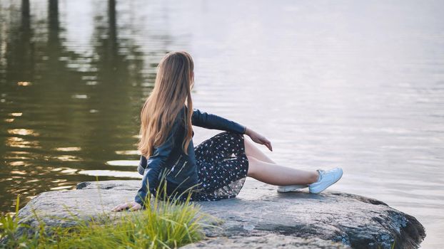 A girl sits by the lake on a rock