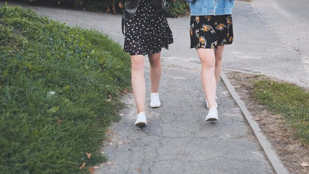 Two girlfriends in white sneakers walk down the street