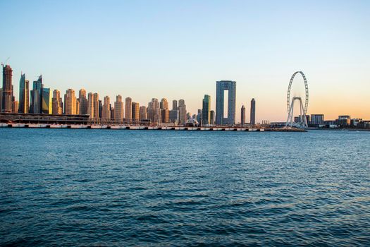 View of A Jumeirah Beach Residence and Blue waters during sunset hour. Shot made from Palm Jumeirah, man made island. Tallest ferris wheel, Ain Dubai can also be seen in the scene Dubai, UAE. Outdoors.